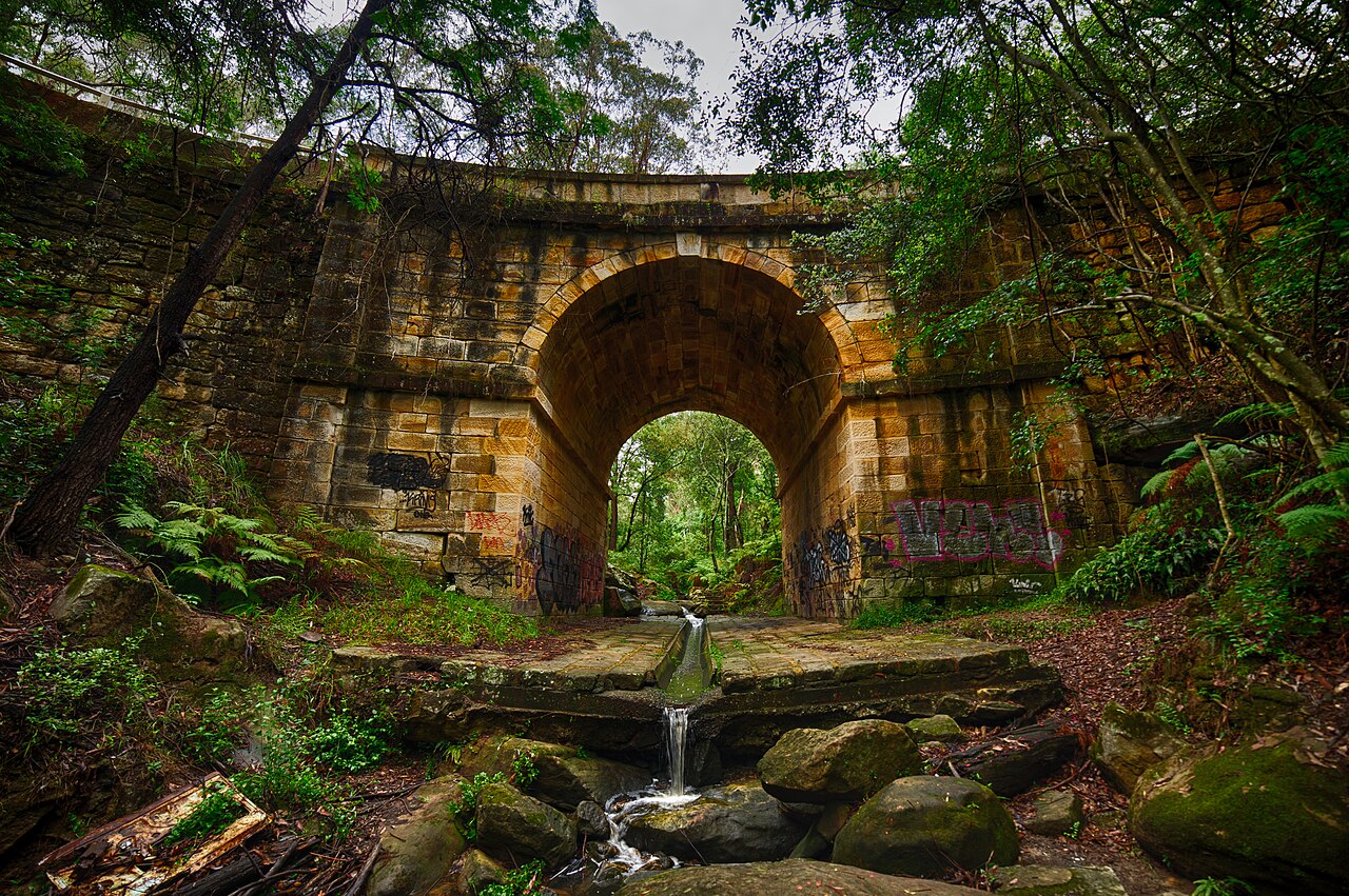 Stone arch of Lennox Bridge with surrounding trees and creek