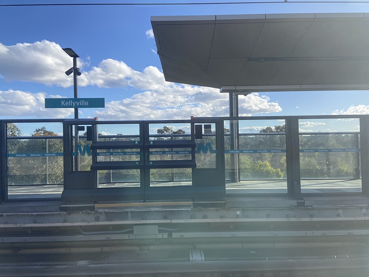 Kellyville Metro platform with its station sign and trees beyond the railway